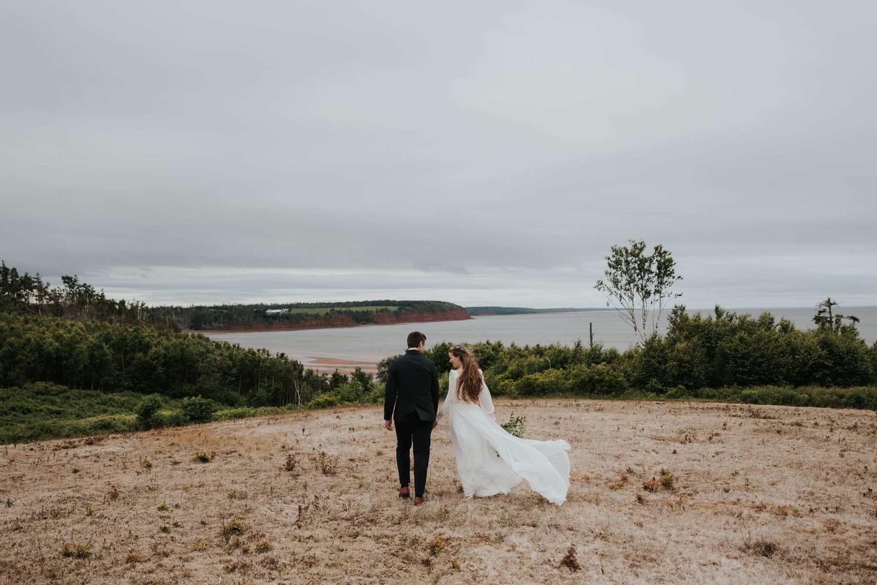 Levi and his wife walking toward the red cliffs and shoreline of Prince Edward Island